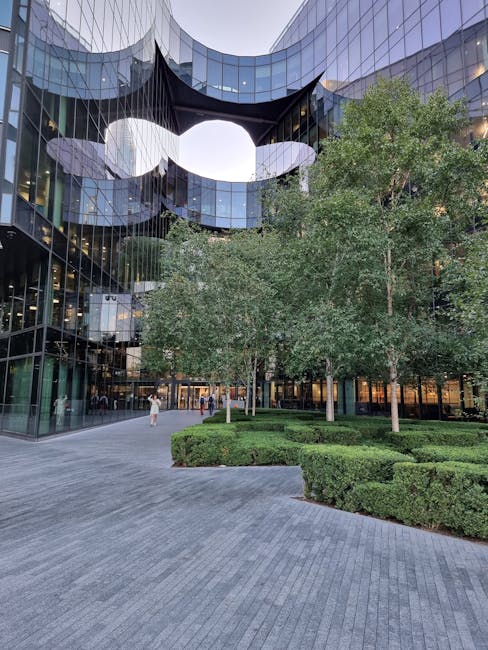 A modern outdoor shopping area near Brent Cross Shopping Centre featuring a paved pedestrian walkway lined with small landscaped garden beds filled with low shrubs and ornamental grasses. The scene sh